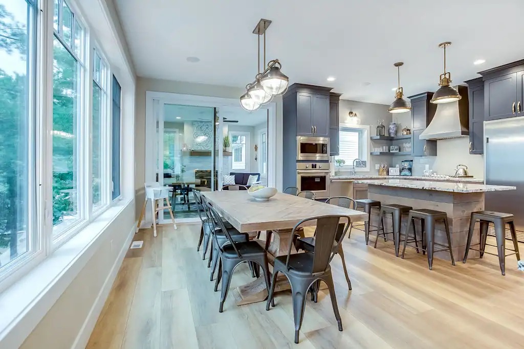 A long dining table seating eight beside a wall of windows — the room the working sessions run in.