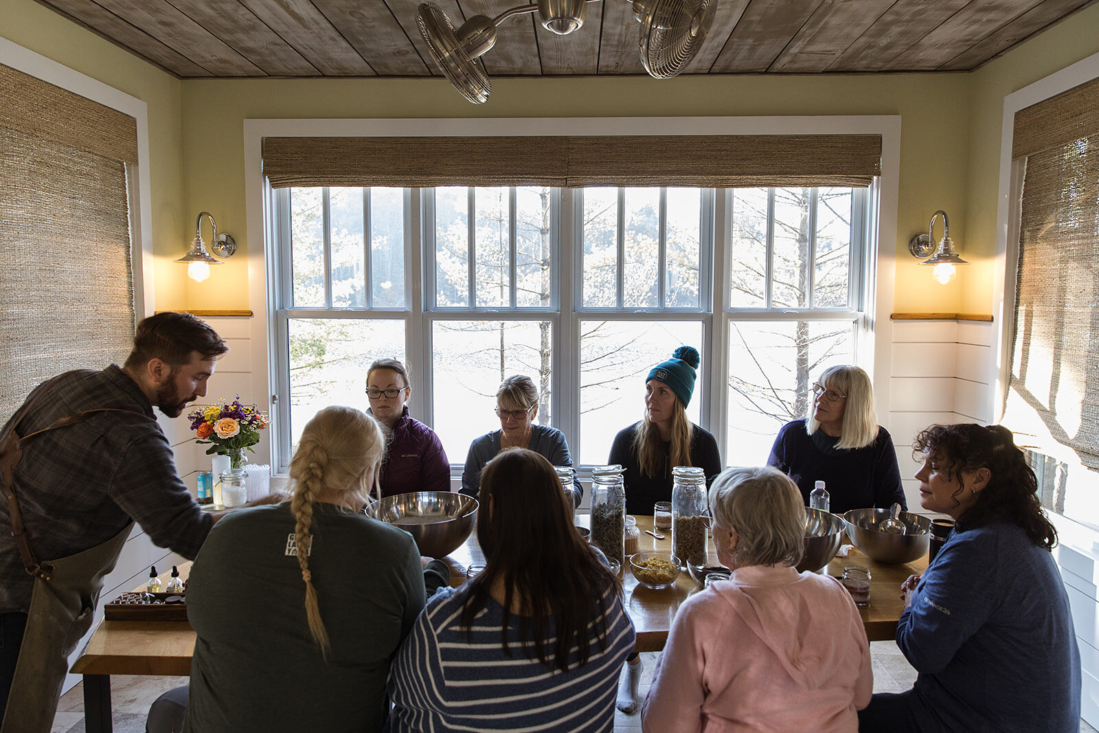 A group seated in a bright porch room with windows on three sides, listening to a session.