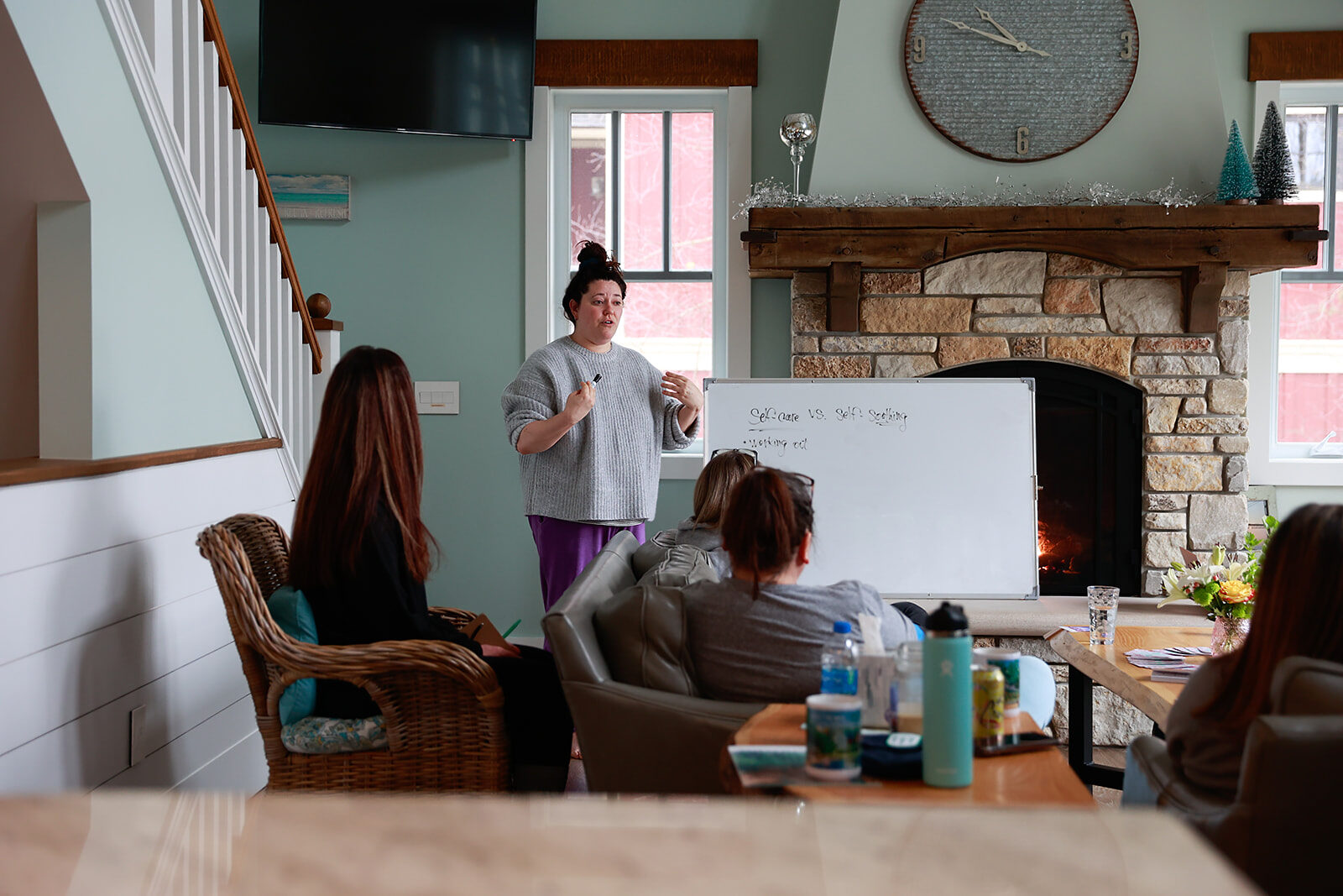 A woman standing at a whiteboard teaching a seated group in a lakehouse living room in winter.