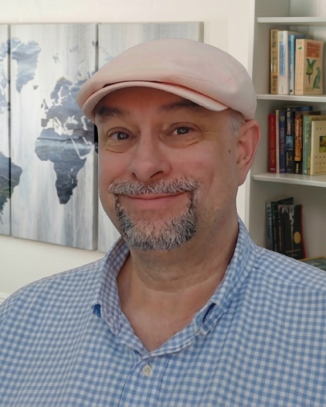 Robert Earl in a flat cap, standing in front of a world map and bookshelves.